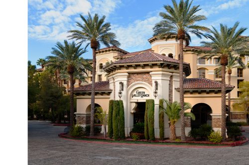 Entrance of Green Valley Ranch resort with Mediterranean-style architecture, palm trees, and clear blue sky.